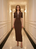 Woman wearing a brown ribbed knit midi dress with white collar trim, standing in a hallway.