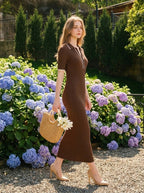 Woman wearing a brown ribbed knit midi dress with white collar trim, carrying a straw bag, walking outdoors near hydrangeas.