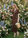 Woman wearing a brown ribbed knit midi dress with white collar trim, reaching for flowers in a garden.