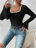 Woman holding a phone, showcasing a black ribbed knit top with detailed sleeves and neckline.
