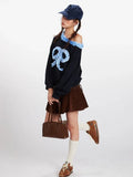 Full body shot of a woman wearing a black off-the-shoulder sweatshirt, brown corduroy pleated mini skirt, white socks, and brown shoes.