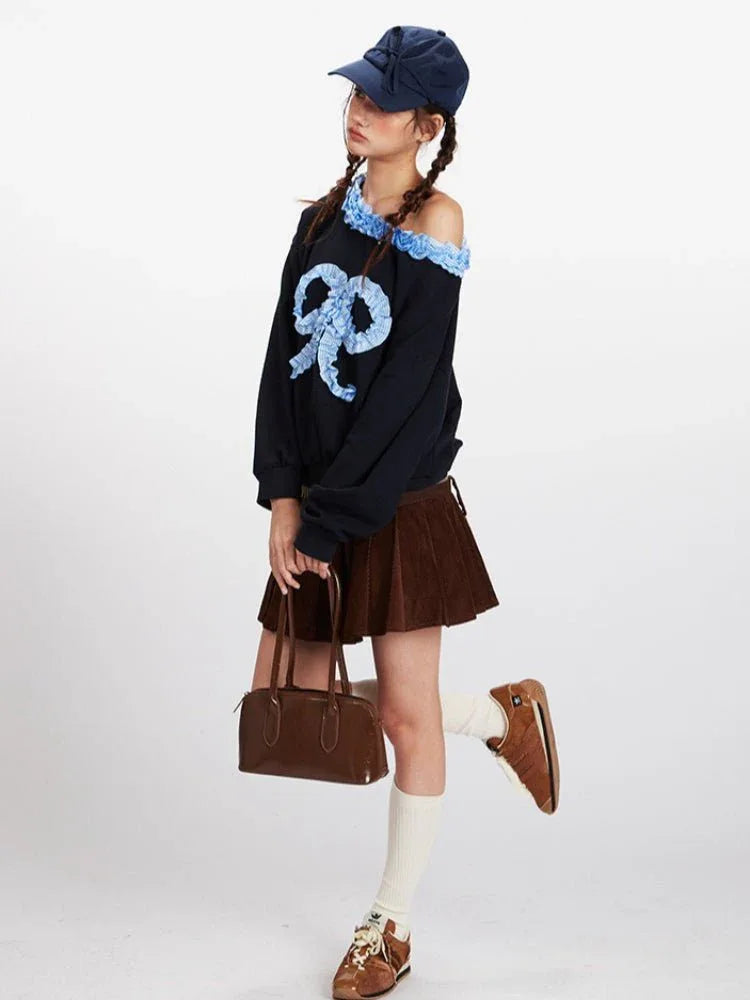 Full body shot of a woman wearing a black off-the-shoulder sweatshirt, brown corduroy pleated mini skirt, white socks, and brown shoes.