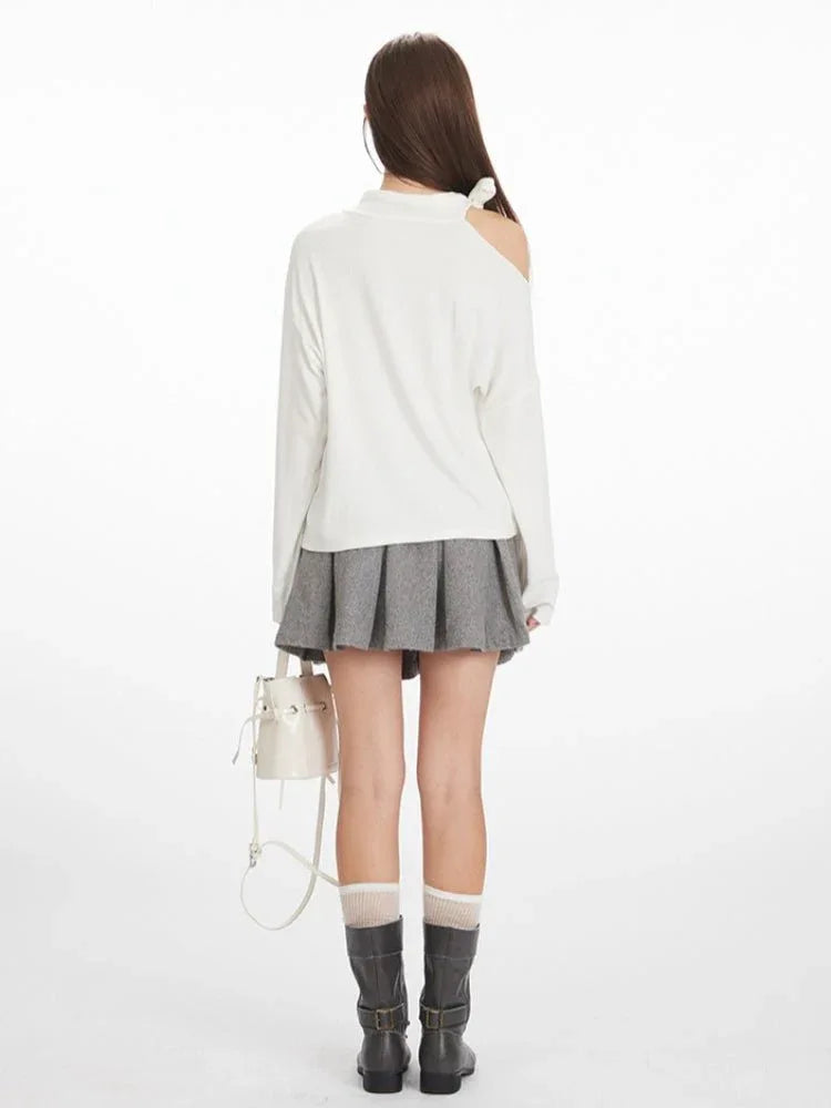 Back view of a woman in a white long-sleeve top and grey pleated skirt, showcasing the full outfit.