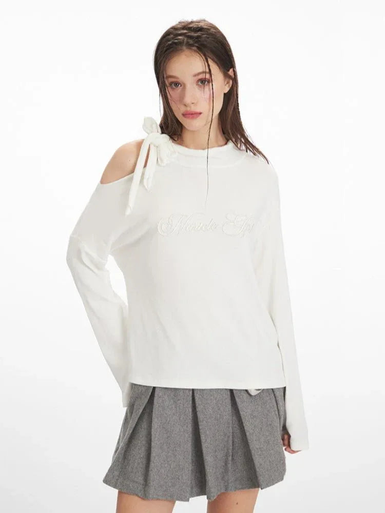 Close-up of the asymmetrical shoulder detail on a white long-sleeve top, showing the bow and cut-out.