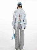 Rear view of a woman in a light blue pinstripe button-down shirt featuring an open back with adjustable ties.