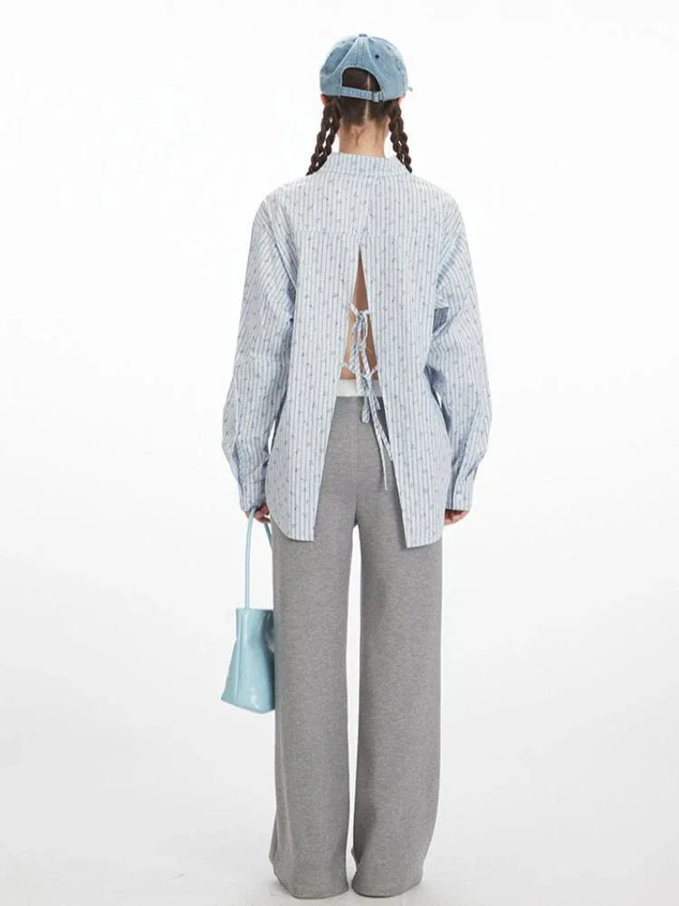 Rear view of a woman in a light blue pinstripe button-down shirt featuring an open back with adjustable ties.