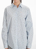 Rear close-up of a woman's back wearing a light blue and white vertical striped long-sleeve shirt with an open back and tie detail, showcasing the intricate tie closure.