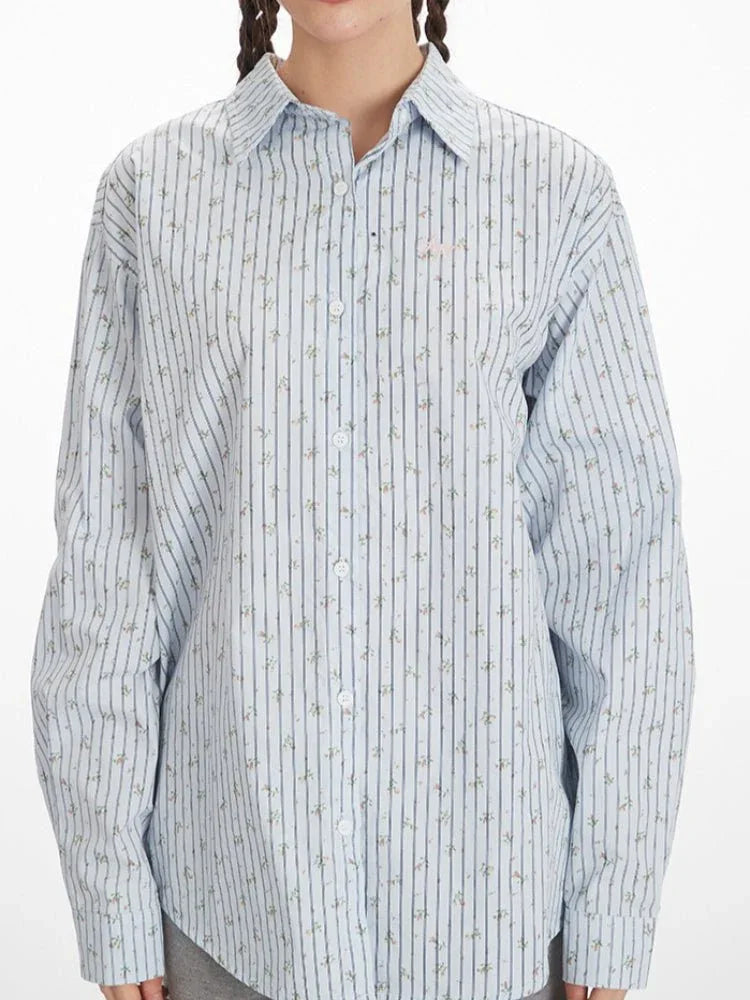 Rear close-up of a woman's back wearing a light blue and white vertical striped long-sleeve shirt with an open back and tie detail, showcasing the intricate tie closure.