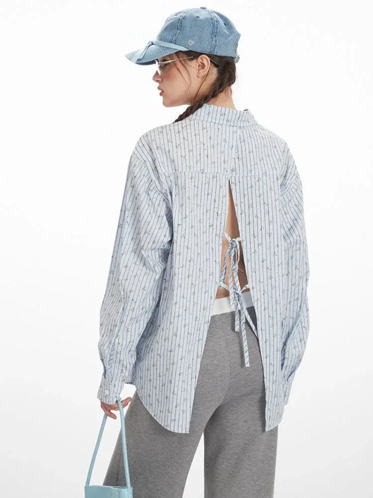 Side view of a woman wearing a light blue and white vertical striped long-sleeve shirt with an open back and tie detail, highlighting the silhouette and back design.