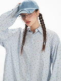 Close-up of a woman's face wearing a light blue pinstripe button-down shirt and a light blue cap, with her hair in braids.