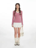 Woman wearing a pink long-sleeve top with white lace trim and white shorts.