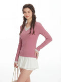 Close-up of a woman's upper body wearing a pink long-sleeve top with V-neck lace detail.