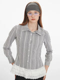 Woman in a plaid long-sleeved collared blouse with lace hem detail, styled with a grey headband and glasses.