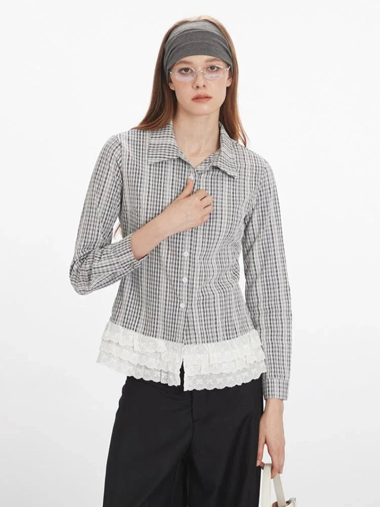 Close-up front view of a woman wearing a long-sleeved collared blouse with a plaid pattern and white lace trim at the hem, showing the button detail.