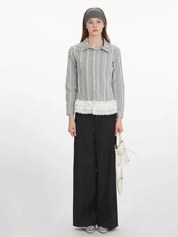 Woman wearing a long-sleeved collared blouse with a plaid pattern and white lace trim at the hem, paired with black wide-leg pants and a white handbag.
