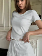 Woman wearing a white short-sleeve crew neck top with ruffled hem and matching white shorts with ruffled waistband