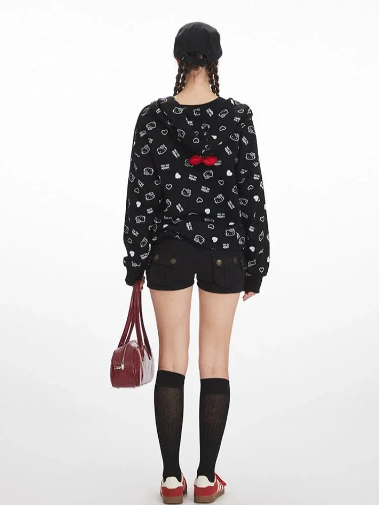Back view of a woman in a black zip-up hoodie with a repeating white Hello Kitty and heart graphic print, black shorts, and knee-high socks.