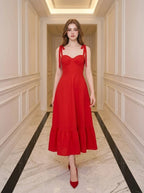Woman in a red midi dress with sweetheart neckline and tie straps walking down a hallway.