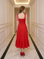 Back view of a woman in a red midi dress with smocked back and ruffle hem.