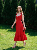 Woman in a red midi dress walking on grass outdoors.