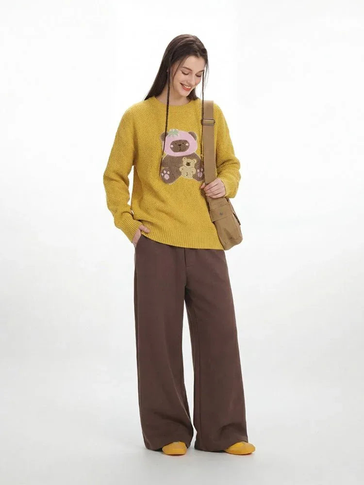 Woman smiling while posing in a yellow teddy bear sweater and brown wide-leg trousers.