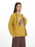 Close-up of the teddy bear appliqué on the yellow knit sweater.