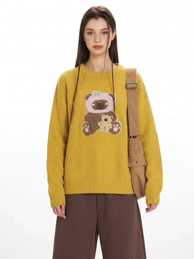 Front view of a yellow knit sweater featuring a teddy bear appliqué on the chest.