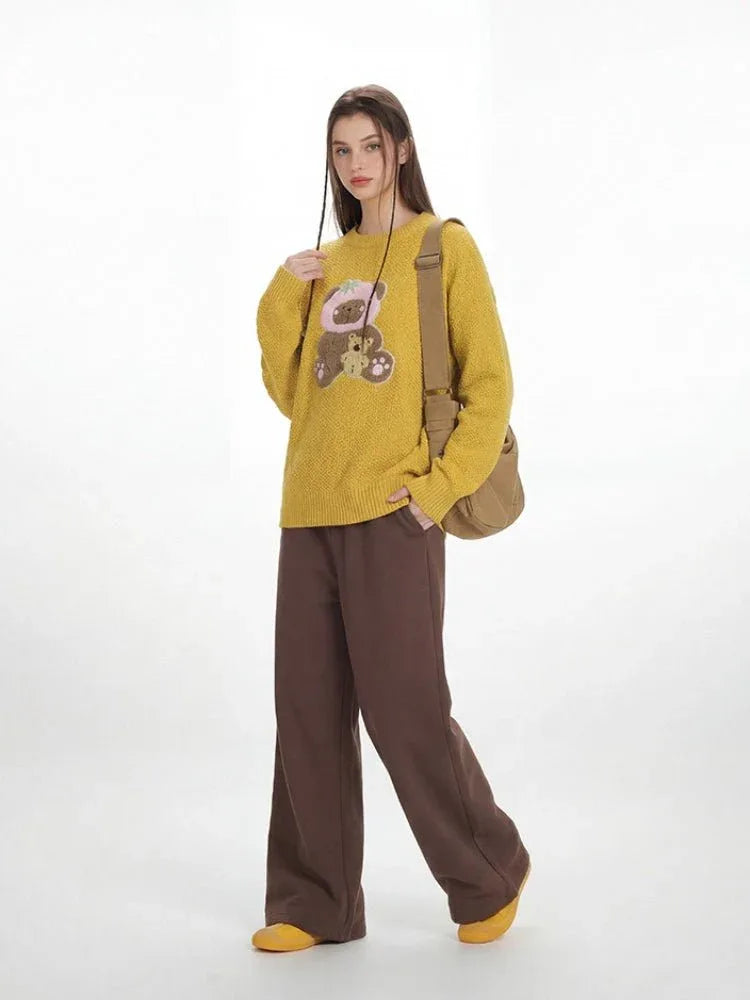 Full-body view of a woman in a yellow teddy bear sweater and brown wide-leg pants.