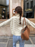 Back view of a woman wearing a cream cable knit turtleneck sweater with light wash jeans and a brown shoulder bag.
