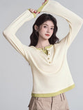 Woman in a cream long-sleeve henley shirt with lime green trim, posing with arms raised.