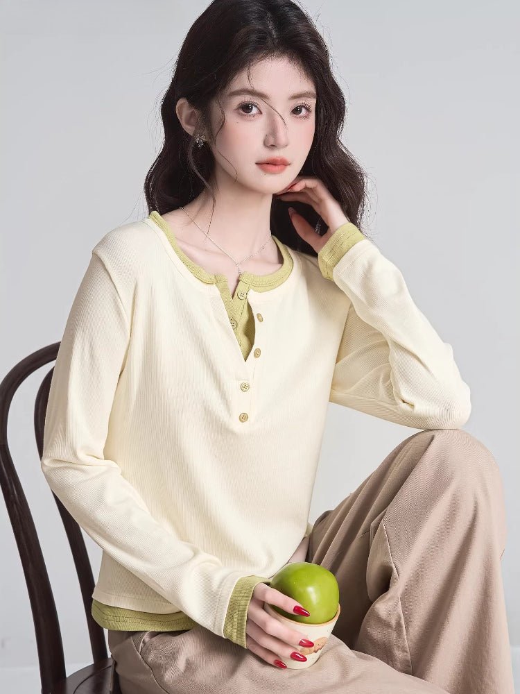 Woman sitting on a chair wearing a cream long-sleeve henley shirt with lime green trim and beige trousers.