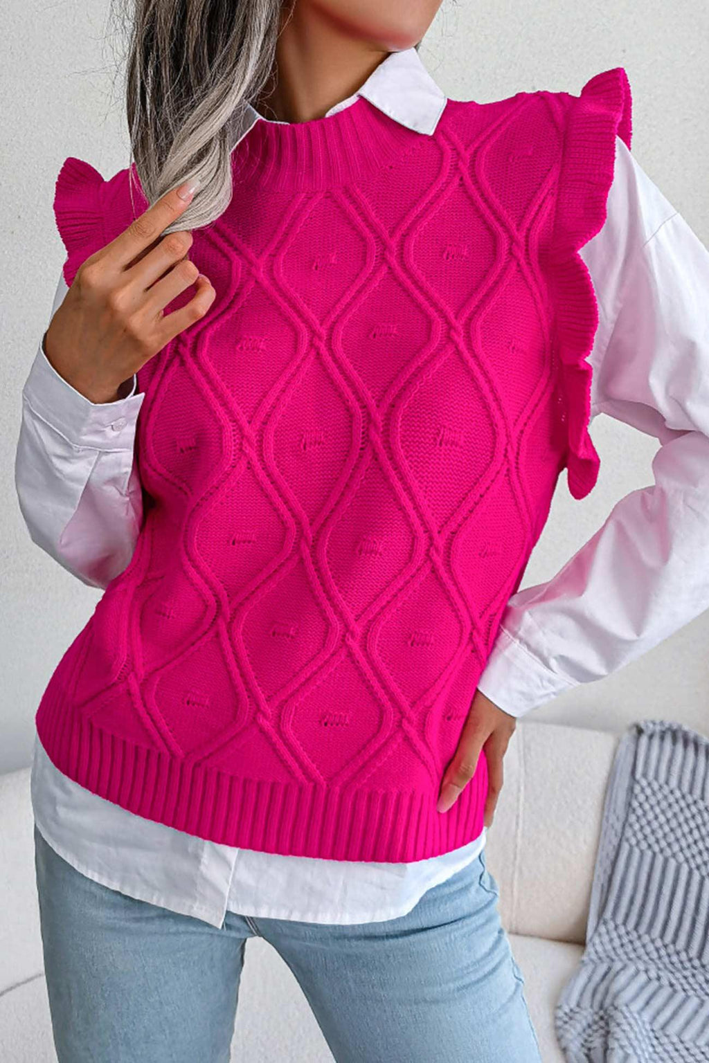 Close-up of a woman wearing a bright pink sleeveless knit vest with a diamond pattern and ruffle trim over a white button-down shirt.