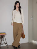 Woman sitting on a chair wearing a cream cable knit sweater and brown pants.