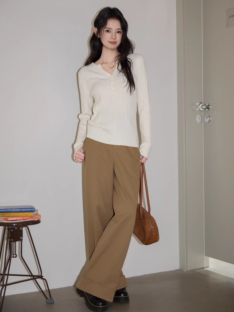 Woman sitting on a chair wearing a cream cable knit sweater and brown pants.