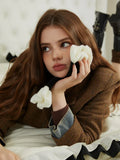 Woman wearing a brown plaid textured jacket, holding a black scarf with white floral accents.