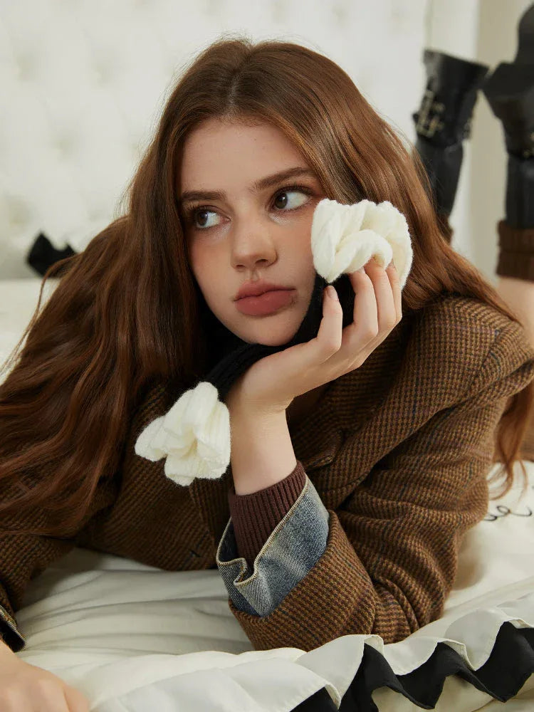 Woman wearing a brown plaid textured jacket, holding a black scarf with white floral accents.