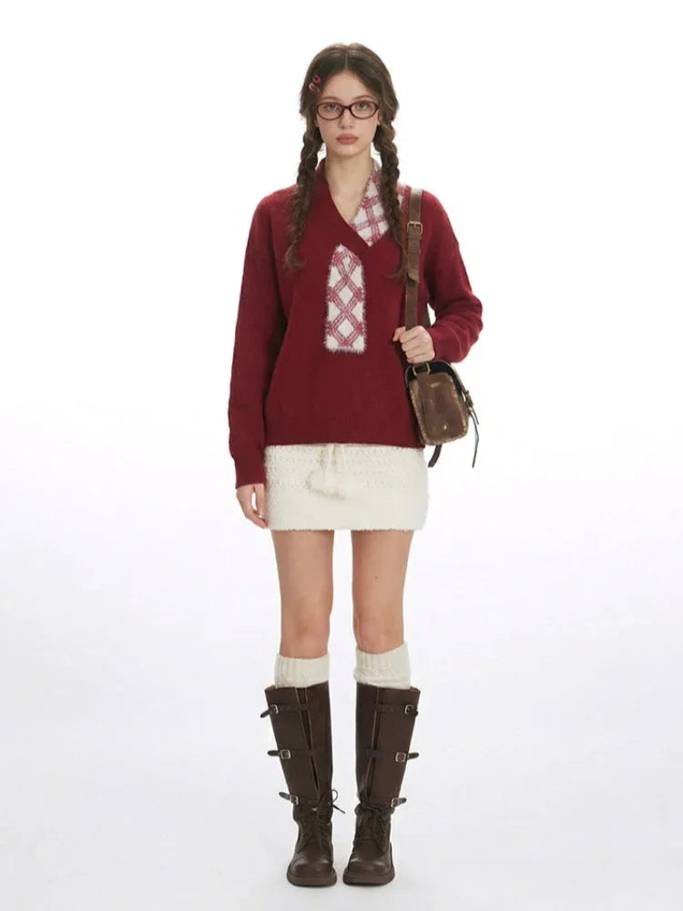 Woman wearing a burgundy V-neck knit sweater with a decorative plaid patch and a white textured mini skirt.