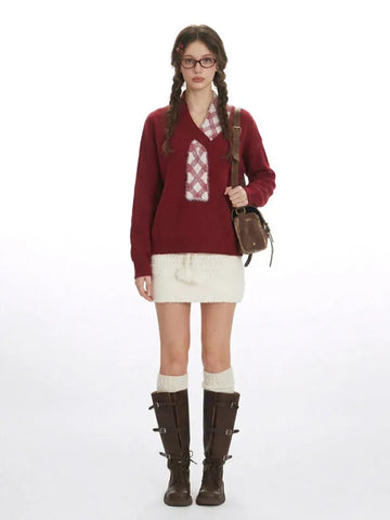 Woman wearing a burgundy V-neck knit sweater with a decorative plaid patch and a white textured mini skirt.