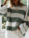 Woman in a green and white striped oversized knit sweater with crew neck and long cuffed sleeves, hand on hip.