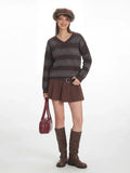 Side profile of a woman wearing a brown striped sweater, brown skirt, and brown boots, holding a red handbag.