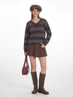 Side profile of a woman wearing a brown striped sweater, brown skirt, and brown boots, holding a red handbag.