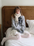 Woman wearing a grey sweatshirt, white ruffled skirt, light pink ribbed tights, and a cream scarf with fringe detail