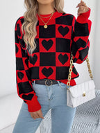 Woman wearing a red and black checkerboard knit sweater with black heart patterns, light wash denim jeans, and a white quilted handbag with a gold chain strap.