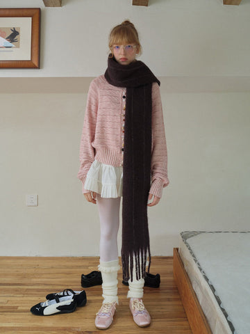 Woman wearing a pink textured knit cardigan with buttons and a dark brown fringe scarf.