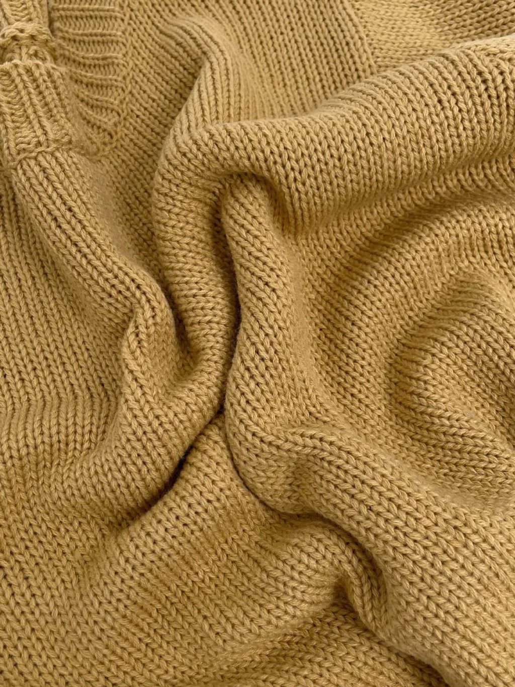 Close-up of the tan chunky knit fabric of the sweater, showing the texture and weave.