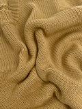 Close-up of the tan chunky knit fabric of the sweater, showing the texture and weave.