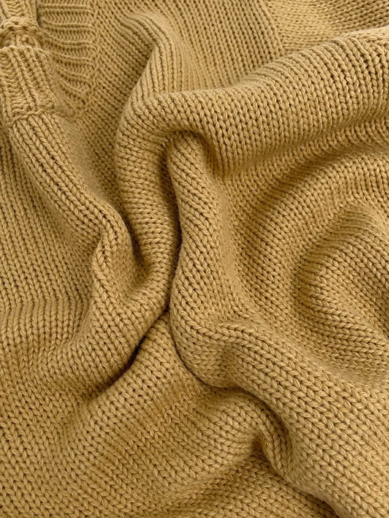 Close-up of the tan chunky knit fabric of the sweater, showing the texture and weave.