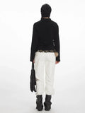 Back view of a woman in a black zip-up fleece jacket, white pants, and black boots.