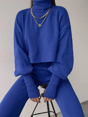 Woman wearing a royal blue knit turtleneck crop top with balloon sleeves and matching royal blue knit pants.