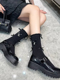 A person wearing black ankle socks with ruffled trim, bows, and pearls, with black platform mary jane shoes and holding a black handbag
